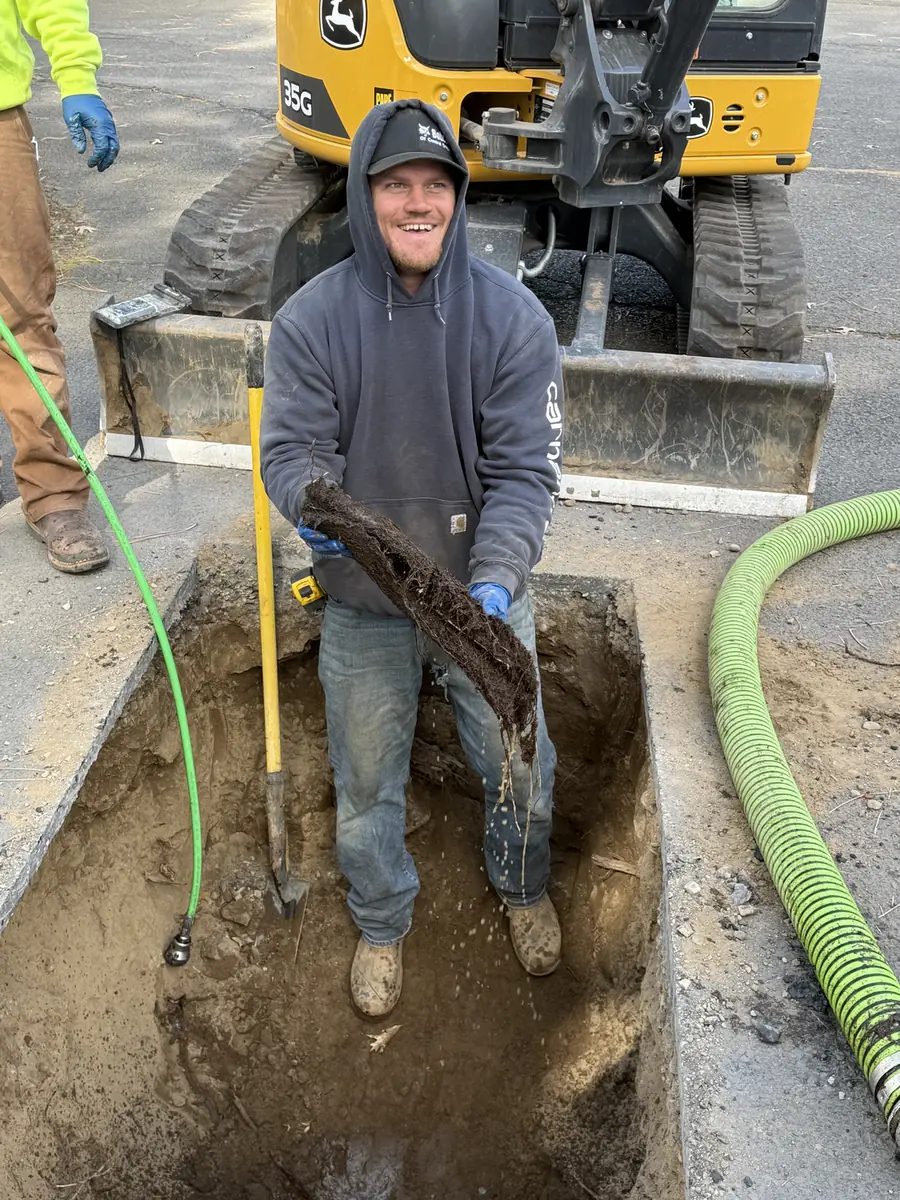 RBE Inc. crew member standing in a freshly dug trench in front of a John Deere mini excavator on a Bend, Oregon job