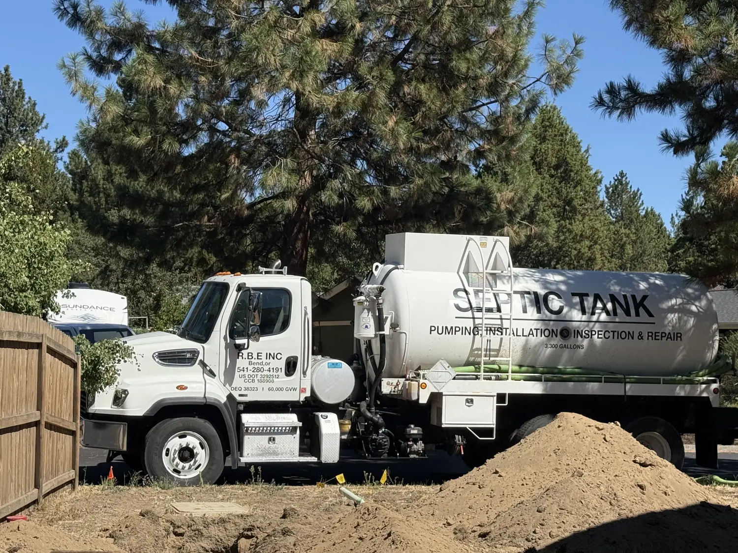 RBE Inc. septic tank truck beside a fresh dirt pile on a Bend, Oregon job site, lettered for pumping, installation, inspection and repair
