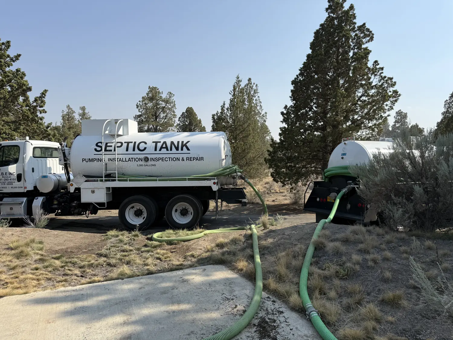 Both RBE Inc. trucks on a Central Oregon job site among junipers, the excavation and septic contractor based in Bend