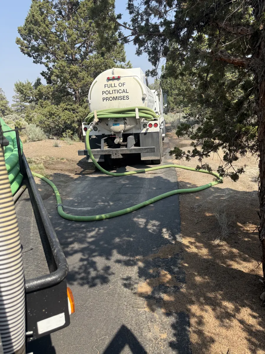 Rear of an RBE Inc. septic pump truck with hoses laid down a juniper-lined driveway near Bend, Oregon