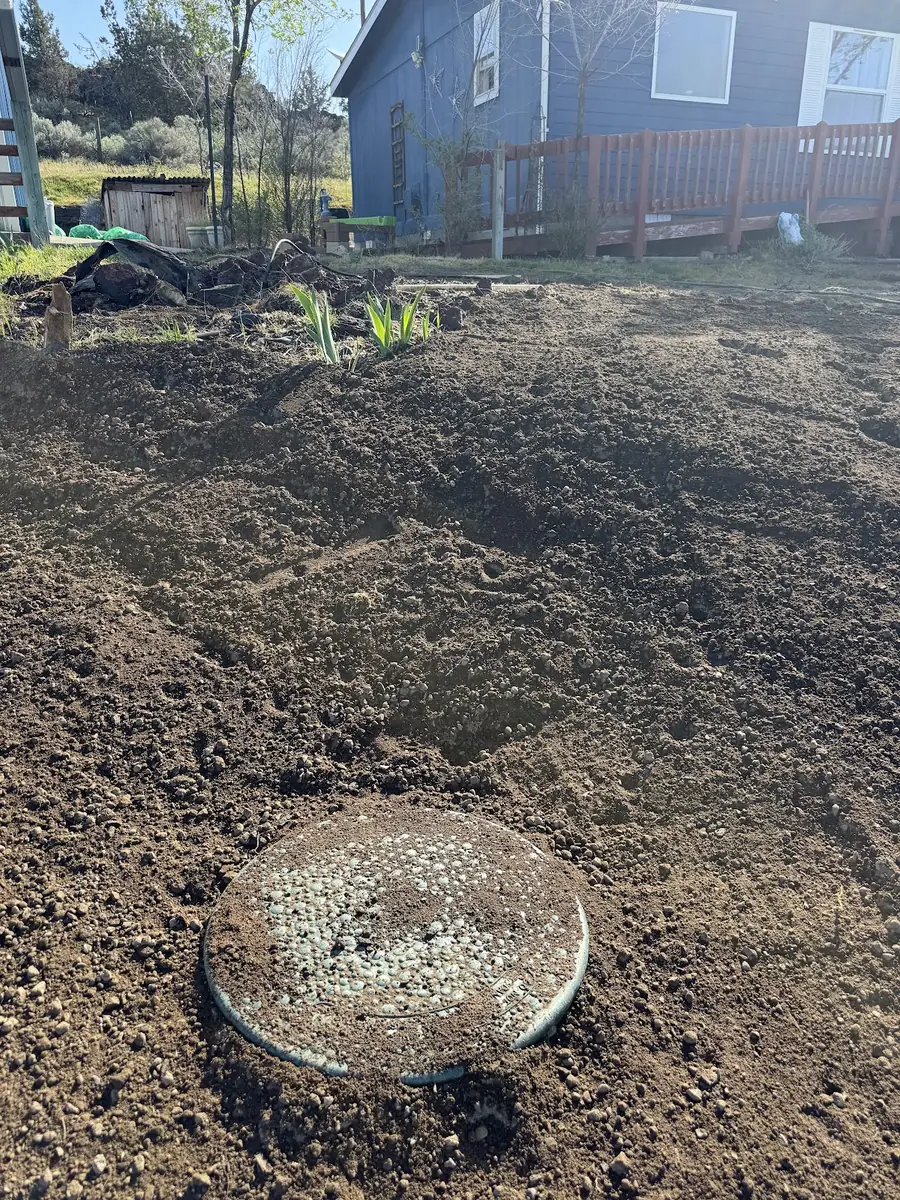 Concrete septic tank lid set at grade in fresh backfill beside a blue house in Bend, Oregon