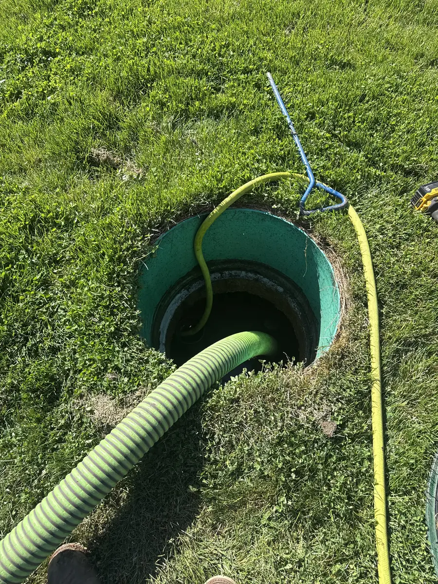 Open green septic tank riser in a lawn with the pump hose inside during a routine pump-out in Bend, Oregon